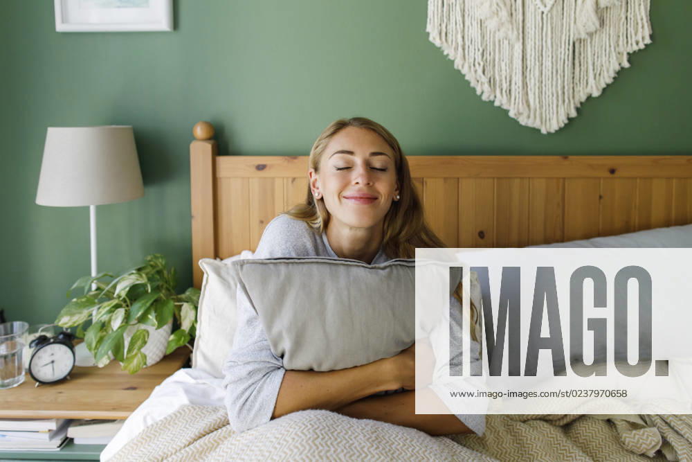 Smiling woman with eyes closed hugging pillow in bed at home model released, Symbolfoto property released, TYF00715