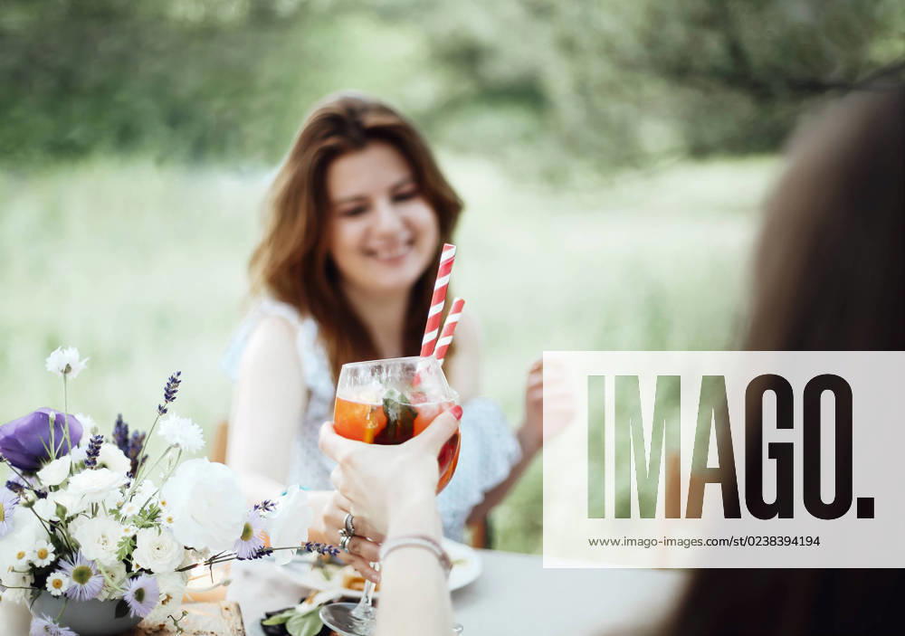 Cheerful woman with cocktail during banquet Happy young female with alcohol cocktail smiling and proposing toast while sitting at table during banquet in garden
