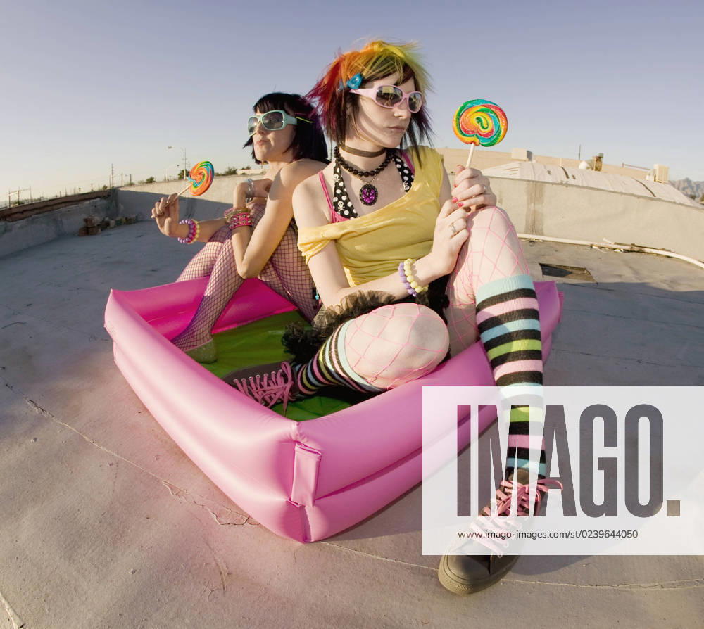 IMAGO Kreativ: Urbane Kultur - Sommer auf den Dächern Fisheye shot of girls in brightly colored clothing in a plastic pool on a roof with sunglasses and lollipops