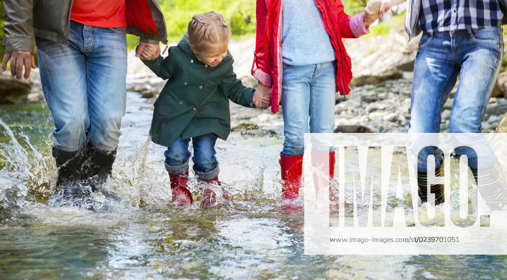 Happy family wearing rain boots jumping into a mountain river Happy family with two children wearing rain boots jumping into a mountain river ,model released, Symbolfoto
