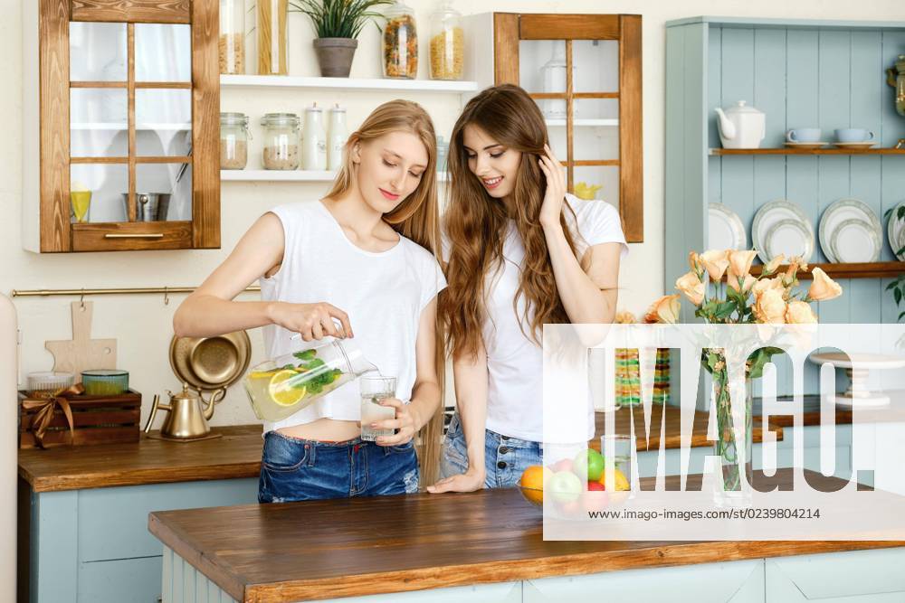 Zwei hübsche Mädchen trinken Limonade und unterhalten sich in der Küche