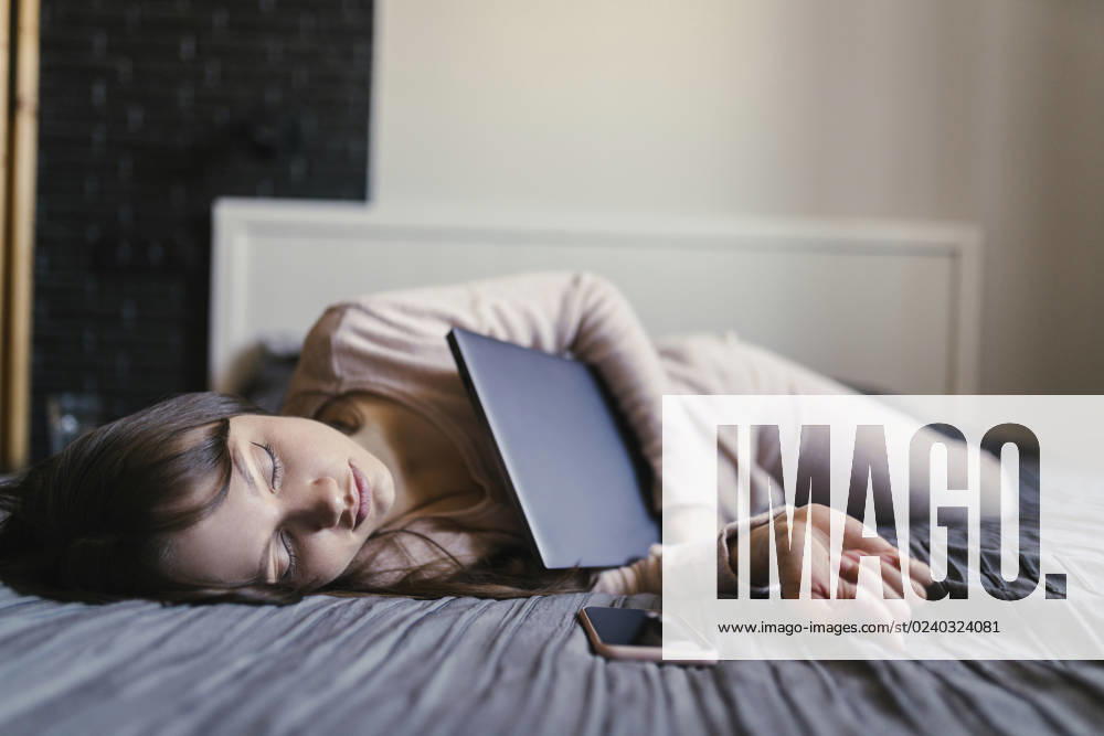Tired freelancer with eyes closed lying on bed holding laptop at home model released, Symbolfoto property released, ANNF00047
