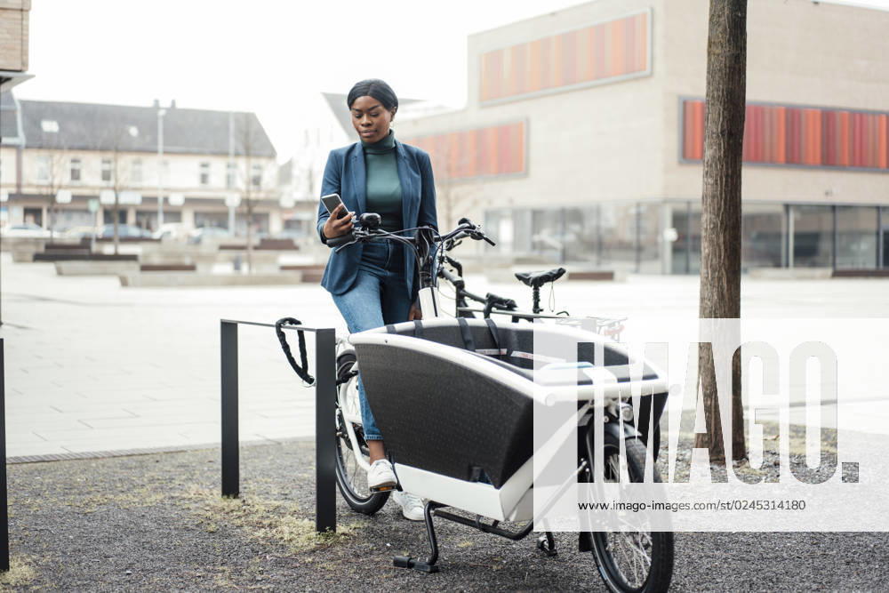 Businesswoman surfing net through smart phone sitting on cargo bike model released, Symbolfoto property released, JOSEF18094