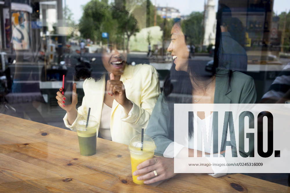 IMAGO Creative, Urban Lifestyle Happy woman talking to friend sitting with juice in cafe seen through window model released, Symbolfoto property released, MMPF00704