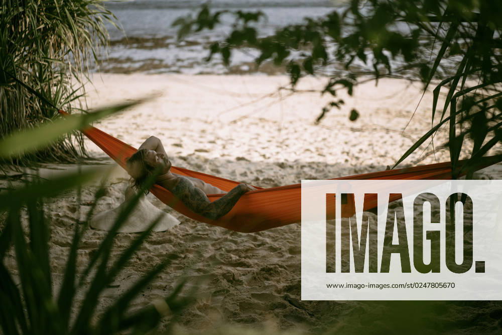 A young man rests and chills in an orange hammock on the beach n Nusa Penida, Bali, Indonesia CR_YUKI230221-1130717-01 ,model released, Symbolfoto ,property released