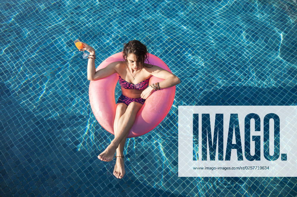 Woman holding drink floating in swimming pool at sunny day model released, Symbolfoto, IKF00258