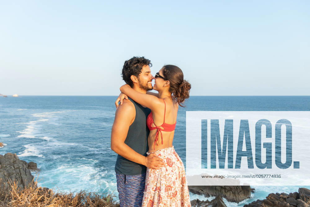 MR_ID13682_13316_EduardoGavira.jpg, MR_ID13682_13317_SamanthaLaguna.jpg Side view of cheerful young couple in summer wear standing on rocky coast and hugging while smiling and enjoying vacation together against waving sea in Puerto Escondido, Model released EduardoGavira_ID13682_415175_018