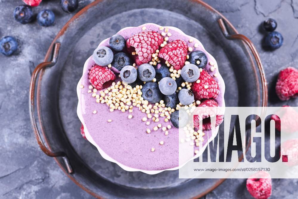 Frucht Smoothie Bowl mit rosa Joghurt, dekoriert mit gesunder Himbeere, Blaubeere und gepufftem Quinoa Korn auf Eisentablett