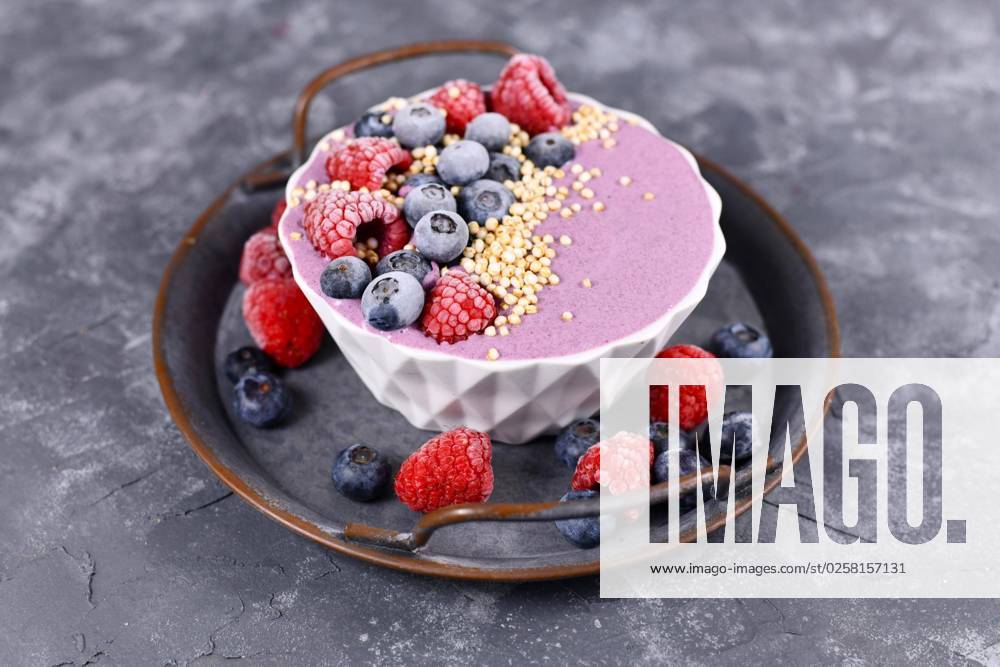 Frucht Smoothie Bowl mit rosa Joghurt, dekoriert mit gesunder Himbeere, Blaubeere und gepufftem Quinoa Korn auf Eisentablett