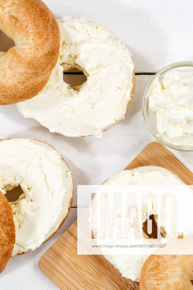 Bagel Brötchen Sandwich zum Frühstück belegt mit Frischkäse auf Holzbrett von oben Hochformat in Stuttgart, Deutschland Stuttgart, Deutschland - 18. März 2023: Bagel Brötchen Sandwich zum Frühstück belegt mit Frischkäse auf Holzbrett von oben Hochformat in Stuttgart, Deutschland.