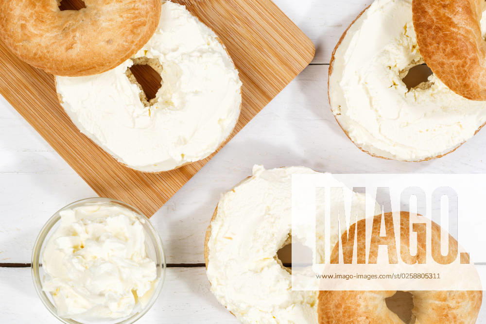 Bagel Brötchen Sandwich zum Frühstück belegt mit Frischkäse auf Holzbrett von oben in Stuttgart, Deutschland Stuttgart, Deutschland - 18. März 2023: Bagel Brötchen Sandwich zum Frühstück belegt mit Frischkäse auf Holzbrett von oben in Stuttgart, Deutschland.