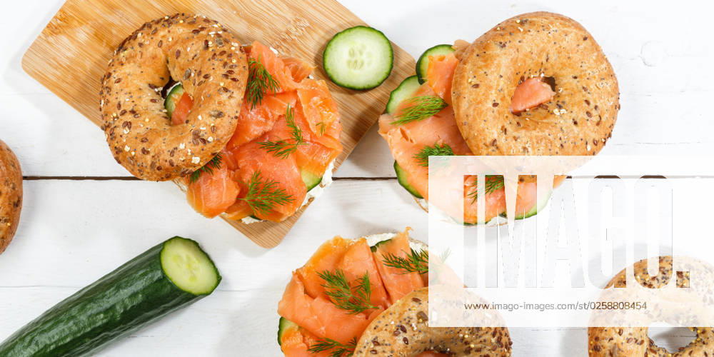 Bagel Brötchen Sandwich zum Frühstück belegt mit Lachs Fisch von oben auf einem Holzbrett Panorama in Stuttgart, Deutschland Stuttgart, Deutschland - 15. März 2023: Bagel Brötchen Sandwich zum Frühstück belegt mit Lachs Fisch von oben auf einem Holzbrett Panorama in Stuttgart, Deutschland.