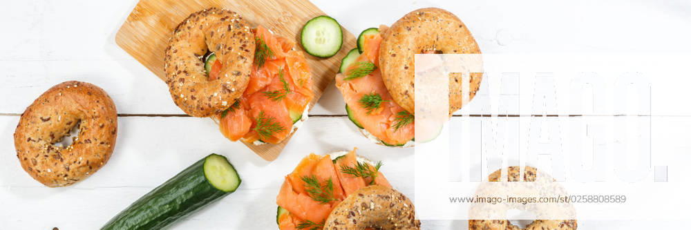 Bagel Brötchen Sandwich zum Frühstück belegt mit Lachs Fisch von oben auf einem Holzbrett Panorama in Stuttgart, Deutschland Stuttgart, Deutschland - 15. März 2023: Bagel Brötchen Sandwich zum Frühstück belegt mit Lachs Fisch von oben auf einem Holzbrett Panorama in Stuttgart, Deutschland.