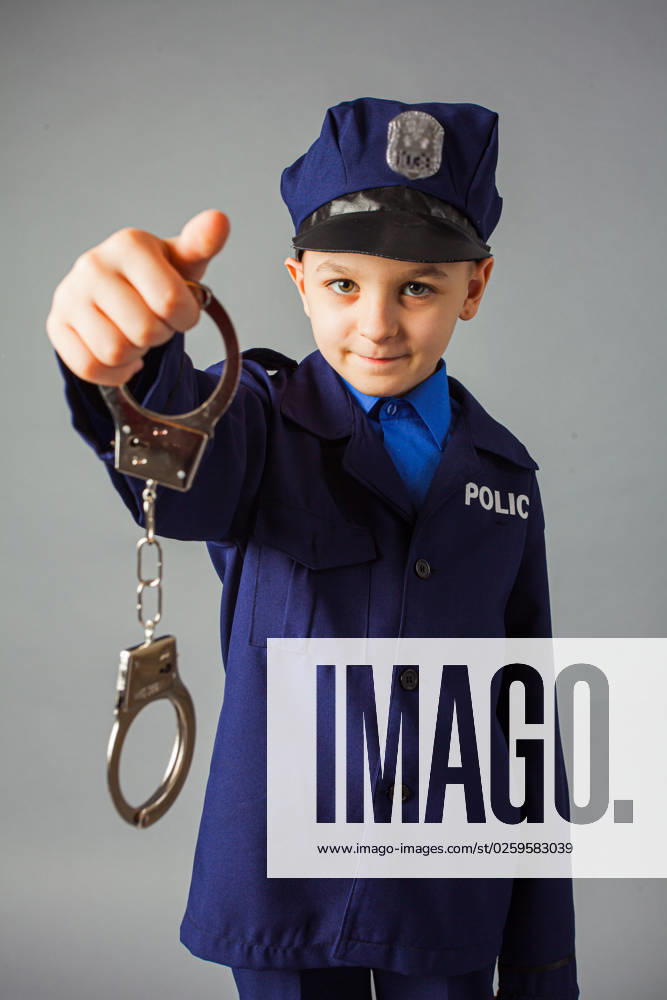 IMAGO Creative, Gesellschaft, Fasching Little boy pretending to be a police officer. Little boy pretending to be a police officer. Cute boy in a policeman costume showing handcuffs over grey background. ,model released, Symbolfoto