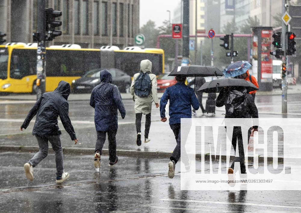 - Menschen in Regenkleidung rennen bei starkem Regenfall ueber einen Fussgaengerueberweg. Starke Unwetter sind ueber Teile Deutschlands gezogen. Berlin Berlin Deutschland