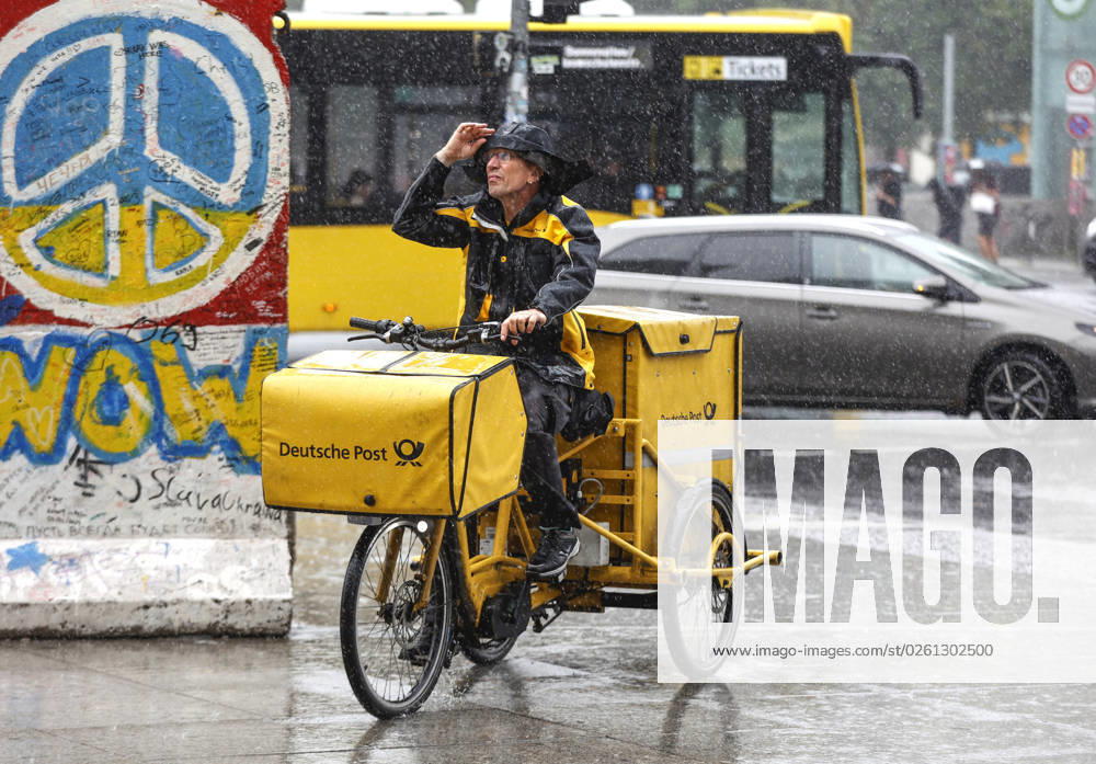 - Ein DHL Briefzusteller faehrt mit seinem E-Bike bei starkem Regen ueber einen Gehweg. Starke Unwetter sind ueber Teile Deutschlands gezogen. Berlin Berlin Deutschland