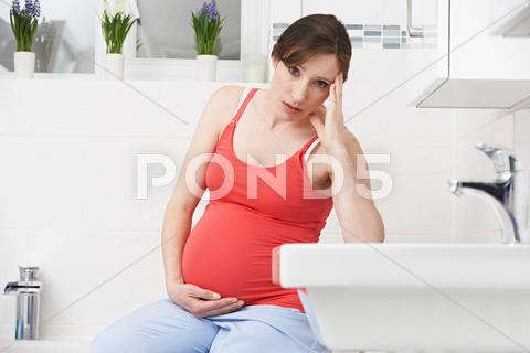 Pregnant Woman Suffering With Morning Sickness In Bathroom 30, at home, bathroom, belly, bump, caucasian, holding, horizontal, ill, illness, indoors, looking at camera, maternity, morning sickness, nausea, one person, people, person, portrait, pregnancy, pregnant, sad, sitting, stomach, thirties, touching, toxicosis, unhappy, unwell, woman, women