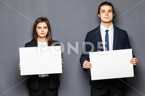 Confident business couple standing with blank board to advertise or invite on gray background background, woman, business, hand, love, person, girl, couple, man, school, banner, paper, young, isolated, space, happy, blank, showing, board, female, male, casual, studio, smile, presentation, white, billboard, guy, job, feeling, portrait, work, copy, together, posing, surprised, product, caucasian, camera, boyfriend, relationship, romantic, expression, presenting, adult, gesture, two, people, message, invitation