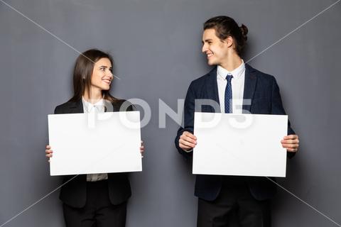 Confident business couple standing with blank board to advertise or invite on gray background background, woman, business, hand, love, person, girl, couple, man, school, banner, paper, young, isolated, space, happy, blank, showing, board, female, male, casual, studio, smile, presentation, white, billboard, guy, job, feeling, portrait, work, copy, together, posing, surprised, product, caucasian, camera, boyfriend, relationship, romantic, expression, presenting, adult, gesture, two, people, message, invitation