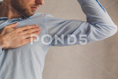 Man with hyperhidrosis sweating very badly under armpit in blue shirt, on grey armpit, hyperhidrosis, sweating, shirt, blue, man, under, sweat, wet, body, person, stain, problem, spot, sweaty, deodorant, arm, excessive, patch, stink, young, embarrassment, hygiene, hand, disgust, background, perspiration, heat, white, hot, underarm, showing, smell, worry, condition, adult, pit, soaked, human, wear, manager, people, gesture, expression, smelling, health, clothing