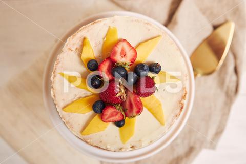 An overhead shot of delicious mango strawberry summer naked cake on a white table with white background cake, sweet, dessert, white, bakery, snack, gourmet, baked, cream, bake, homemade, pastry, background, cooking, closeup, holiday, delicious, eat, fresh, sugar, decoration, birthday, party, piece, table, tasty, naked, mango, strawberry, summer