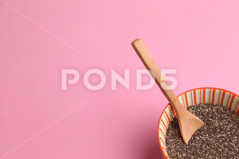 A closeup of a bowl filled with chia seeds, with a wooden spoon on a pink surface food, healthy, organic, wooden, spoon, grain, diet, raw, seed, chia, natural, vegetarian, brown, seeds, health, ingredient, bowl, vegan, wood, background, dried, dry, colours, breakfast, table, antioxidant, closeup, pink, surface
