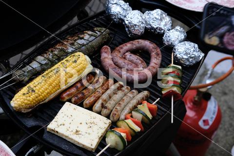 A high angle shot of seasoned vegetables on skewers, sausages, cheese and stuffed fish on a grill vegetables, fresh, food, nutrition, ingredient, pepper, onion, cucumber, epicure, paprika, slices, meal, cheese, eat, corn, ear, seed, sausages, meat, pork, product, tasty, stuffed, fish, dish, filled, preparation, seafood, snack, cooking, barbecue, delicious, wooden, skewers, salt, seasonings, aromatic, top, herb, flavoring, various, spices, gourmet, preparing, grill, heat, bbq, piece