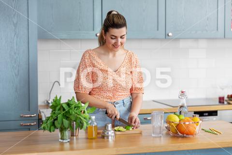Culinary and people concept - happy smiling young woman making cocktail drinks with lime and peppermint at home kitchen {woman,drink,lemonade,cocktail,making,lime,knife,cutting,kitchen,home,mixologist,glass,beverage,mojito,recipe,ingredient,bar,citrus,drinking,refreshment,non-alcoholic,mocktail,alcohol,chopping,fruit,mint,peppermint,happy,smiling,homemade,craft,housewife,hobby,preparing,process,young,beautiful,nice,hispanic,person,people,table,concept,adult,30s,indoors}