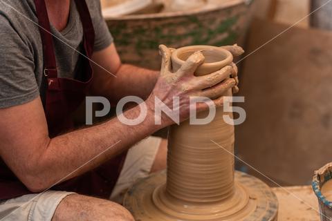 Crop unrecognizable sculptor with equipment giving shape while sculpting with brown clay on throwing wheel man, shape, clay, sculpt, equipment, process, motion, jug, ceramic, skill, male, sculptor, workshop, art, artist, handicraft, earthenware, ceramist, craft, create, dirty, form, hobby, handmade, maker, master, molding, occupation, pottery, utensil, wet, wheel, professional, work, artisan, throw, small business, talent, workplace, crop, unrecognizable, faceless, anonymous, horizontal, body part, blur, indoors