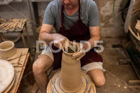 Crop unrecognizable sculptor with equipment giving shape while sculpting with brown clay on throwing wheel man, shape, clay, sculpt, equipment, process, motion, jug, ceramic, skill, male, sculptor, workshop, art, artist, handicraft, earthenware, ceramist, craft, create, dirty, form, hobby, handmade, maker, master, molding, occupation, pottery, utensil, wet, wheel, professional, work, artisan, throw, small business, talent, workplace, crop, unrecognizable, faceless, anonymous, horizontal, body part, blur, indoors