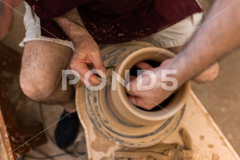 Crop unrecognizable sculptor with equipment giving shape while sculpting with brown clay on throwing wheel man, shape, clay, sculpt, equipment, process, motion, jug, ceramic, skill, male, sculptor, workshop, art, artist, handicraft, earthenware, ceramist, craft, create, dirty, form, hobby, handmade, maker, master, molding, occupation, pottery, utensil, wet, wheel, professional, work, artisan, throw, small business, talent, workplace, crop, unrecognizable, faceless, anonymous, horizontal, body part, blur, indoors, top view, from above
