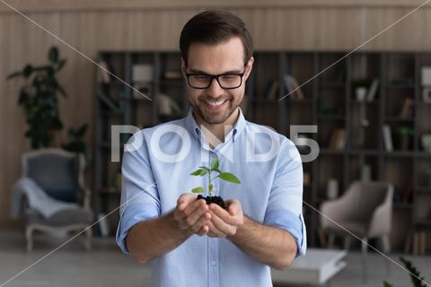 Smiling businessman wearing glasses holding small green plant sprout with soil, standing, happy entrepreneur employee with growing tree, startup project, profit, investment and growth concept man, people, person, concept, business, businessman, entrepreneur, employee, glasses, happy, good, smile, future, growing, symbol, holding, protection, natural, development, sprout, plant, green, soil, leaf, tree, growth, earth, environment, care, seedling, save, world, ecology, seed, finance, environmental, nature, investor, success, support, professional, executive, small, new, idea, dream, money, profit, wealth