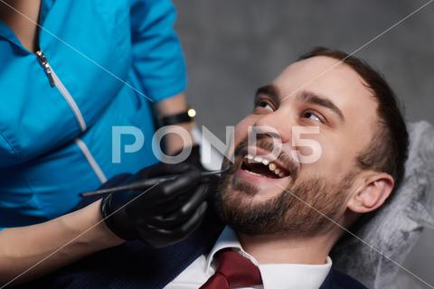 Smiling young man sitting in dentist chair while doctor examining his teeth medical, woman, man, doctor, dentist, tool, specialist, procedure, patient, oral, gloves, examination, health, treatment, clinic, tooth, teeth, dental, medicine, caucasian, equipment, stomatology, visit, mouth, cabinet, checkup, cure, examine, young, uniform, latex, indoors, orthodontist, sterile, protective, mask, dentistry, hospital, toothache, surgical, instrument, hygiene, workplace, heal, operation, inspection, occupation