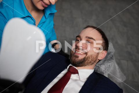 Smiling young man sitting in dentist chair while doctor examining his teeth medical, woman, man, doctor, dentist, tool, specialist, procedure, patient, oral, gloves, examination, health, treatment, clinic, tooth, teeth, dental, medicine, caucasian, equipment, stomatology, visit, mouth, cabinet, checkup, cure, examine, young, uniform, surgical, protective, mask, toothache, latex, operation, hygiene, orthodontist, occupation, dentistry, workplace, indoors, instrument, sterile, heal, hospital, inspection