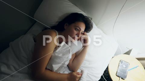 Woman laying in bed at night unable to sleep. Person turning light on in the middle of the night suffering from insomnia feeling stress with ruminating thoughts insomnia,woman,bed,bedroom,home,female,night,young,stress,problem,sleepless,tired,awake,lying,pillow,depression,sleep,sad,headache,disorder,anxiety,people,person,unhappy,girl,adult,worried,clock,beautiful,alone