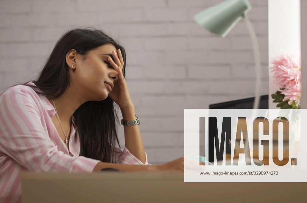 Portrait of a tired woman sitting on desk with hand on head
