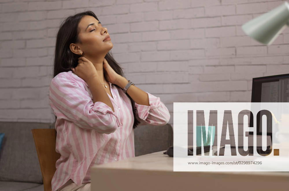 Portrait of a tired woman sitting on desk with hands on neck