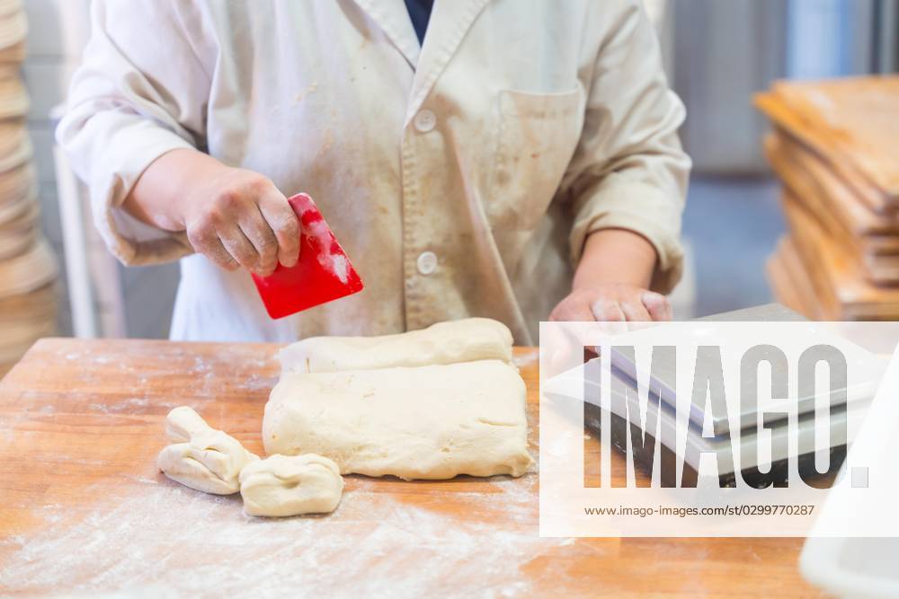 Angestellte eines Brotbackautomaten in der Werkstatt einer handwerklichen Bäckerei beim Schneiden von Teig
