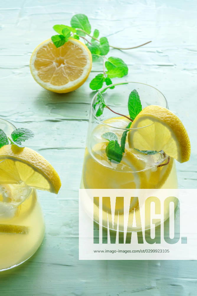 Lemonade with mint. Lemon water drink with ice. Two glasses and a lemon Lemonade with mint. Lemon water drink with ice. Two glasses and a lemon half on a blue background. Detox beverage. Fresh homemade cocktail