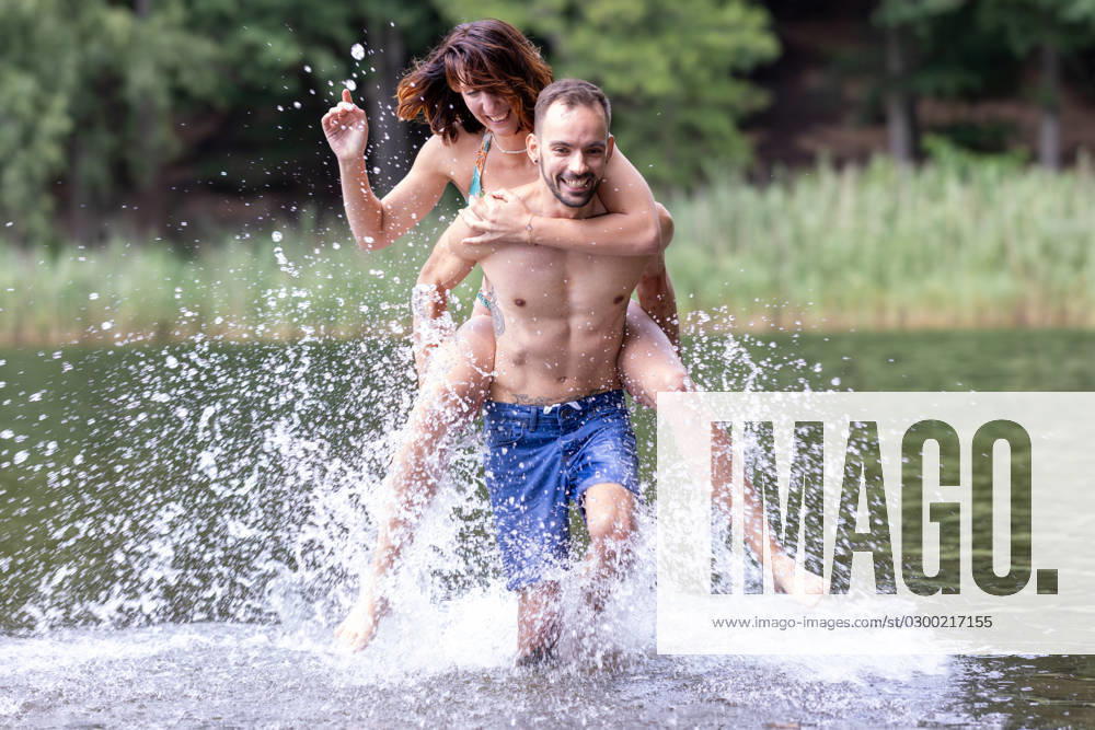 CREATIVE - Paar am See in Berlin Berlin, Deutschland - 25. Juli 2023: (CREATIVE) Ein Mann trägt Huckepack eine Frau (Models) und genießen einen Sommertag an der Krummen Lanke, einem See in Berlin. Berlin