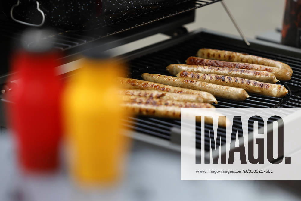 Grillwürste liegen auf einem Kohlegrill. Im Vordergrund Ketchup und Senf. (Themenbild, Symbolbild) Köln, 25.07.2023 NRW Deutschland