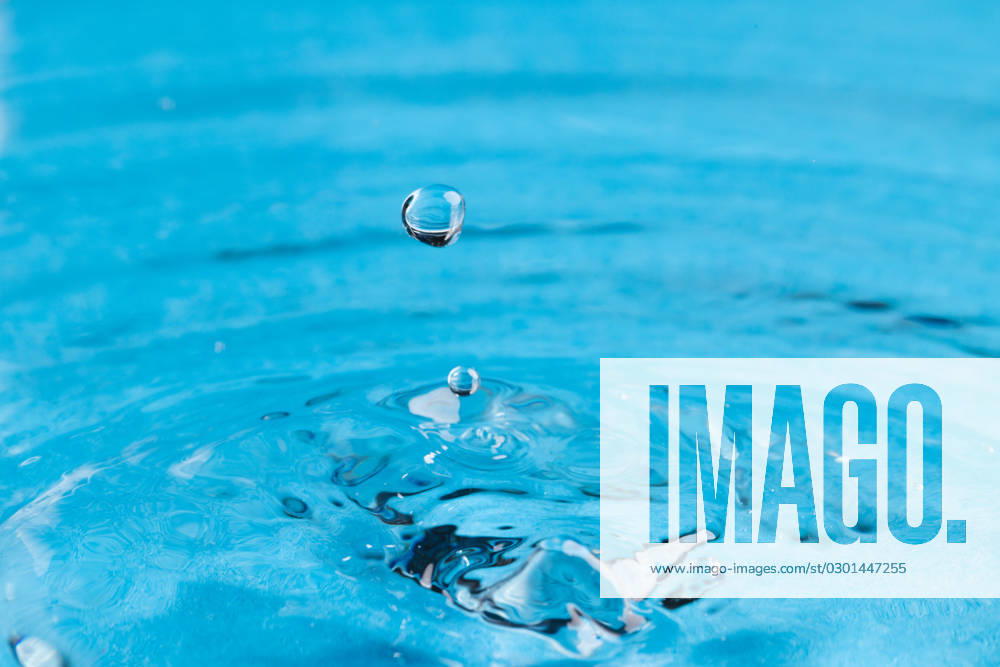 Close up of water drop falling into water with ripples and copy space on blue background. Water, liquid and colour concept.