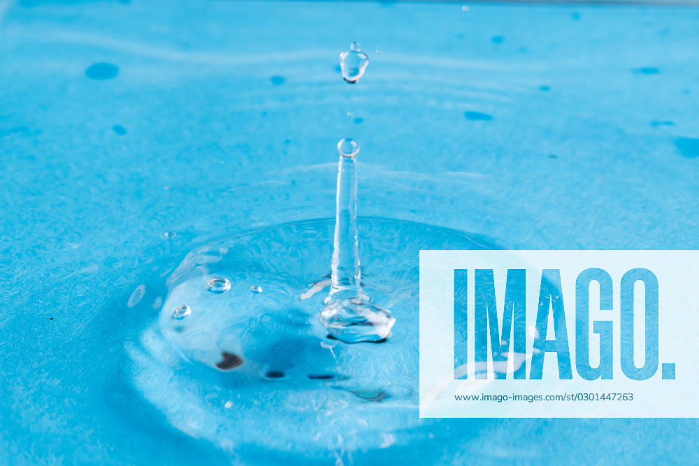 Close up of water drop falling into water with ripples and copy space on blue background. Water, liquid and colour concept.