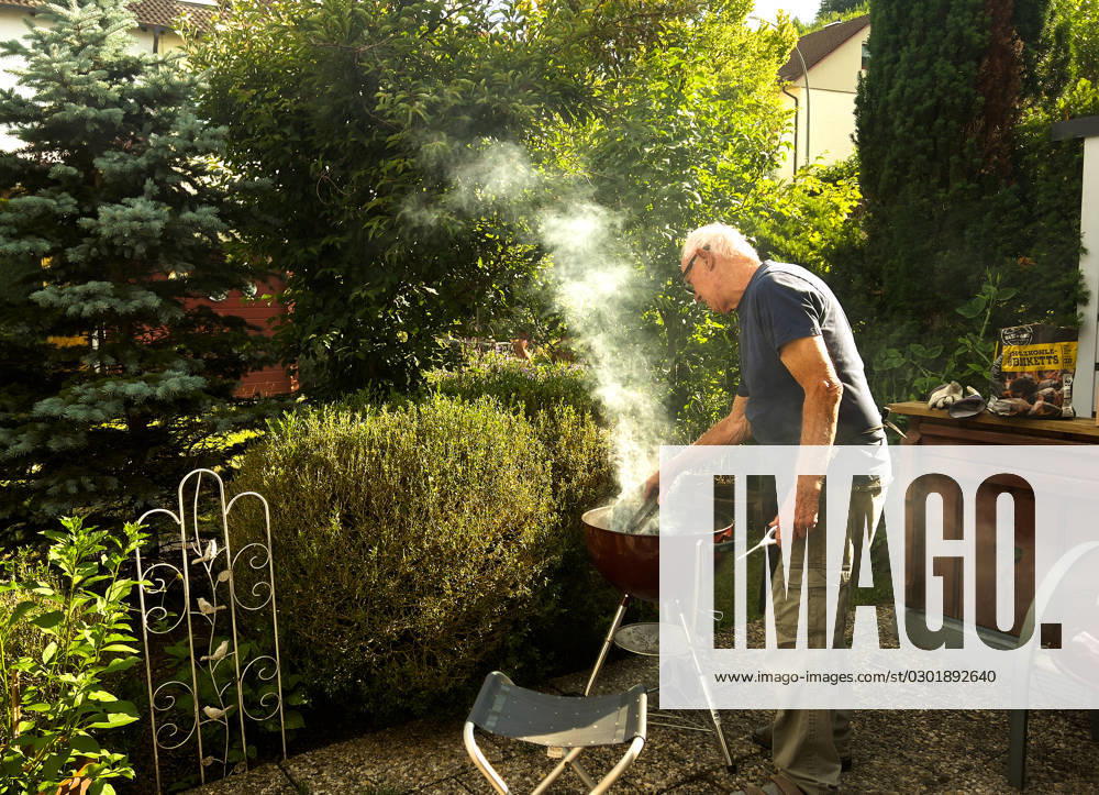 An elderly gentleman lights the charcoal and produces a lot of smoke in Biessenhofen, Bavaria, Germany, July 22, 2023. Model Released
