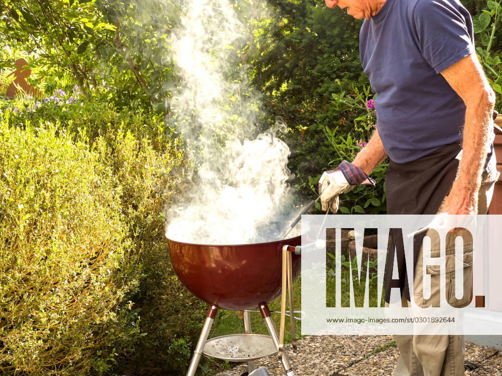 An elderly gentleman lights the charcoal and produces a lot of smoke in Biessenhofen, Bavaria, Germany, July 22, 2023. Model Released