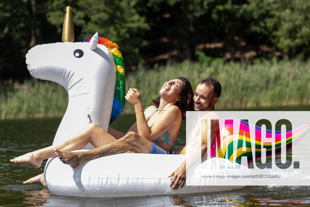 CREATIVE - Paar am See in Berlin Berlin, Deutschland - 25. Juli 2023: (CREATIVE) Ein Mann und eine Frau (Models) genießen auf einem aufgeblasenen Einhorn einen Sommertag an der Krummen Lanke, einem See in Berlin. Berlin