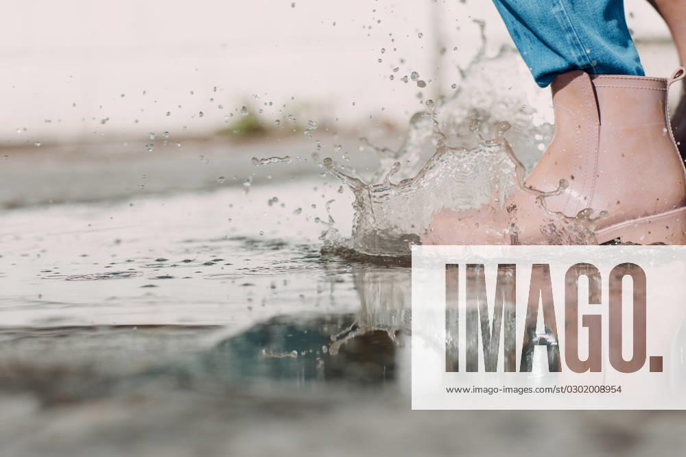 Woman wearing rain rubber boots walking running and jumping into puddle with water splash and drops in autumn rain Woman wearing rain rubber boots walking running and jumping into puddle with water splash and drops in autumn rain. ,model released, Symbolfoto
