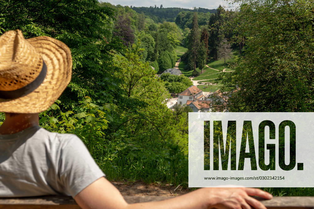Woman with straw hat sitting on a park bench in the sun, looking at Staatspark Fürstenlager, Auerbach, Bensheim Woman with straw hat, gray t-shirt and jeans sitting on a wooden park bench in the sun, looking at Staatspark Fürstenlager, Auerbach, Bensheim, Germany ,model released, Symbolfoto
