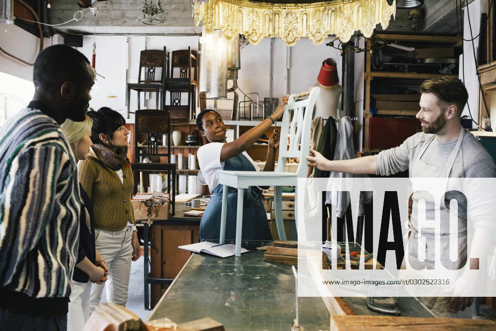 Male and female entrepreneurs showing upcycled wooden chair to customers at workshop Germany, Berlin, model released, property released
