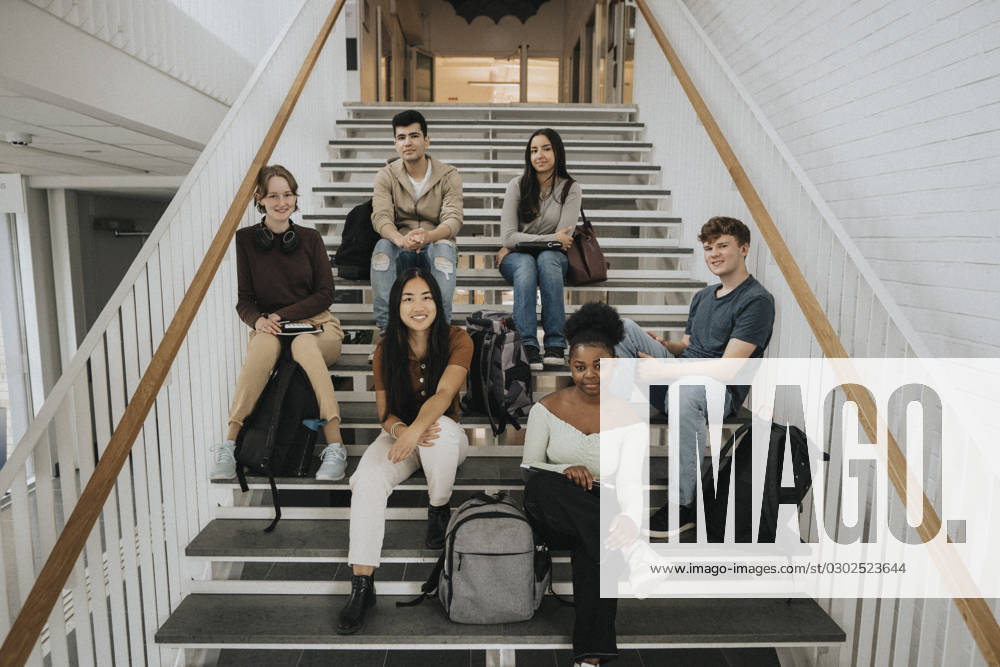 Portrait of happy multiracial male and female students sitting on staircase in university Sweden, Gothenburg, model released, property released